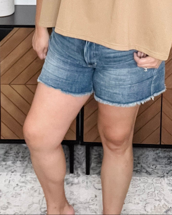 Woman standing in a room with wooden cabinets and decorative plants.